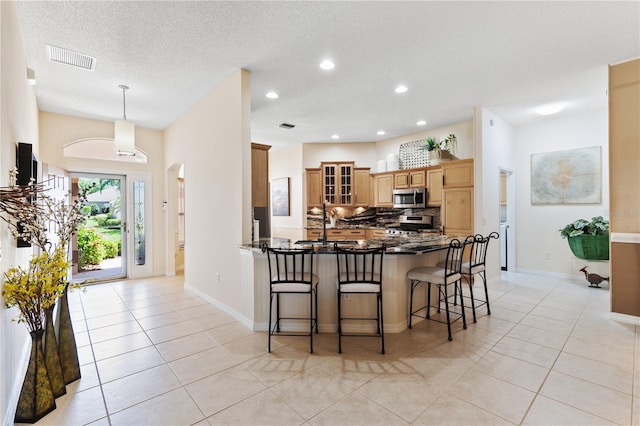 kitchen with a kitchen breakfast bar, a peninsula, visible vents, decorative backsplash, and stainless steel appliances