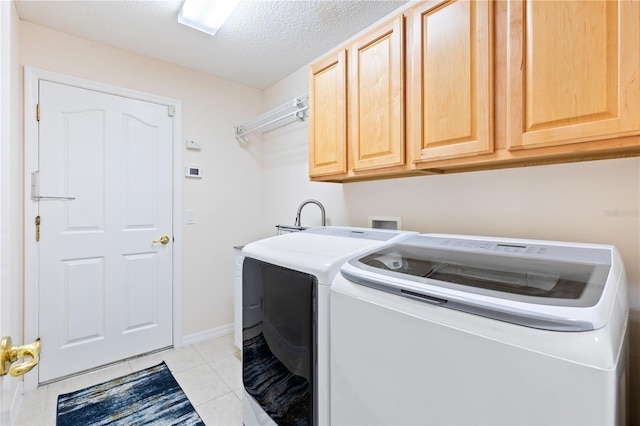 clothes washing area featuring baseboards, light tile patterned floors, a textured ceiling, cabinet space, and washing machine and clothes dryer