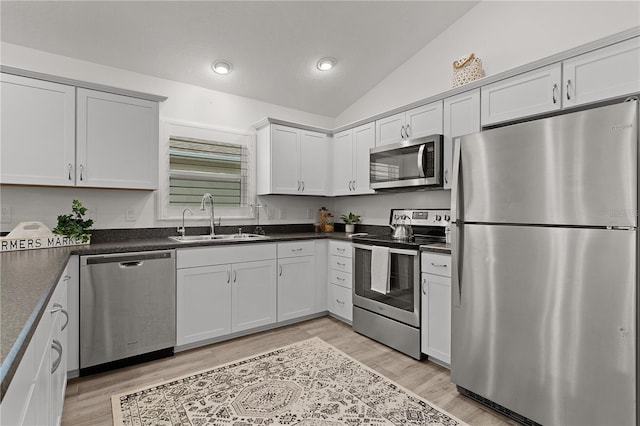 kitchen with light wood-style floors, vaulted ceiling, appliances with stainless steel finishes, a sink, and dark countertops