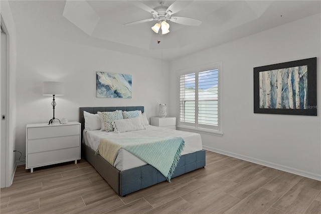bedroom featuring a tray ceiling, light wood-type flooring, baseboards, and a ceiling fan