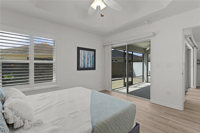 bedroom with light wood finished floors, access to exterior, baseboards, and a raised ceiling