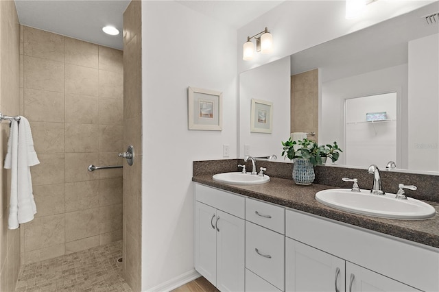 full bathroom with a sink, visible vents, a tile shower, and double vanity