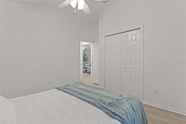 bedroom with ceiling fan, high vaulted ceiling, light wood-style flooring, a closet, and baseboards