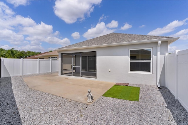 rear view of property featuring stucco siding, a patio area, a fenced backyard, a sunroom, and a shingled roof