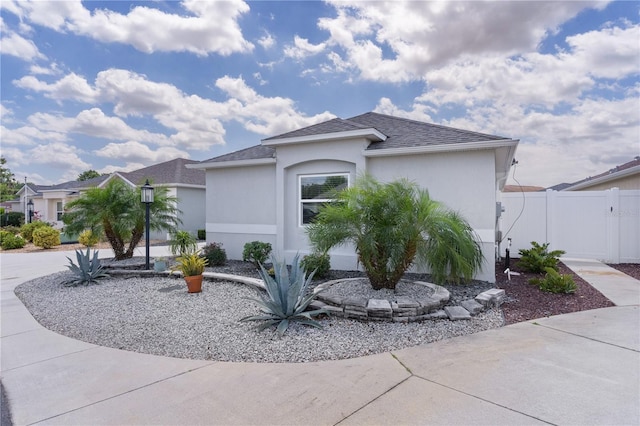 view of front of house featuring roof with shingles, concrete driveway, stucco siding, and fence