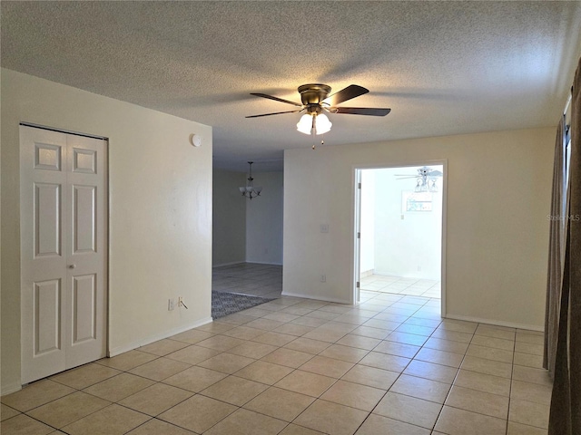 spare room with light tile patterned floors, ceiling fan with notable chandelier, baseboards, and a textured ceiling