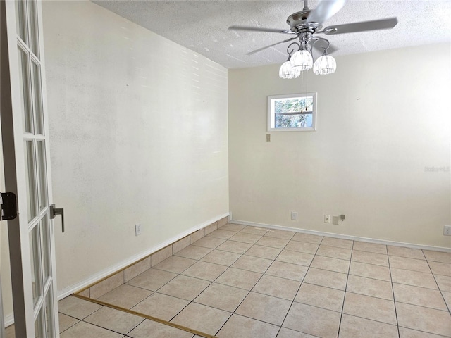 unfurnished room with ceiling fan, light tile patterned flooring, baseboards, and a textured ceiling
