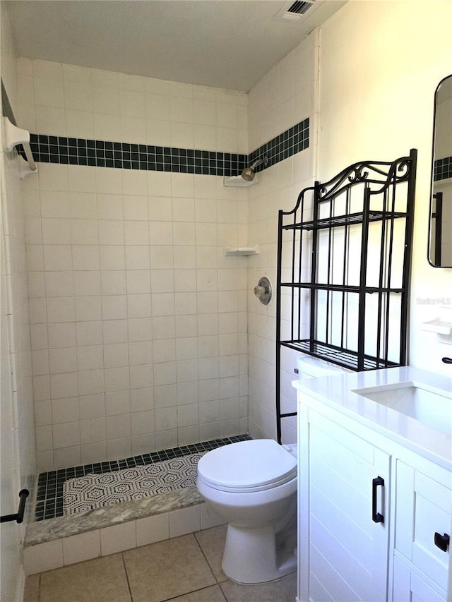bathroom featuring a tile shower, vanity, tile patterned flooring, visible vents, and toilet