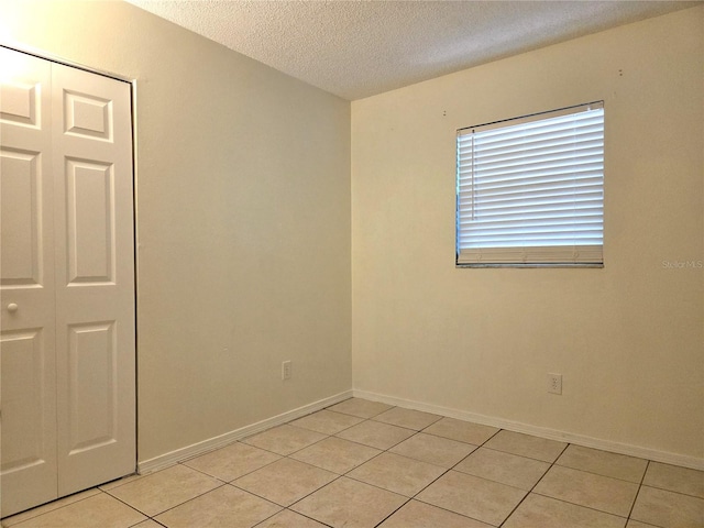 unfurnished room featuring light tile patterned floors, a textured ceiling, and baseboards