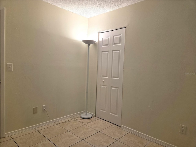 unfurnished room with a textured ceiling, light tile patterned flooring, and baseboards