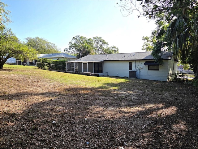 back of house with fence, central AC, concrete block siding, a sunroom, and a lawn