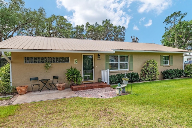 back of property featuring a yard, a patio area, metal roof, and stucco siding