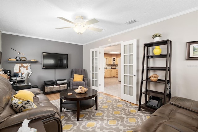 living area featuring light wood-type flooring, french doors, crown molding, visible vents, and ceiling fan