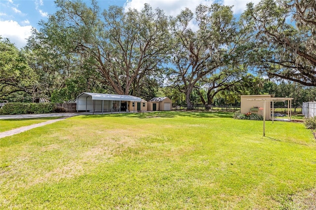view of yard with a carport, fence, and an outdoor structure