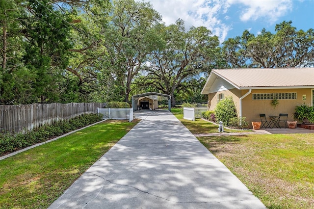 view of home's community with concrete driveway, a carport, fence, and a lawn