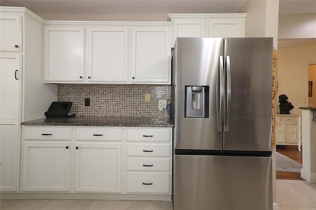 kitchen featuring white cabinets, stainless steel refrigerator with ice dispenser, tasteful backsplash, and dark stone counters