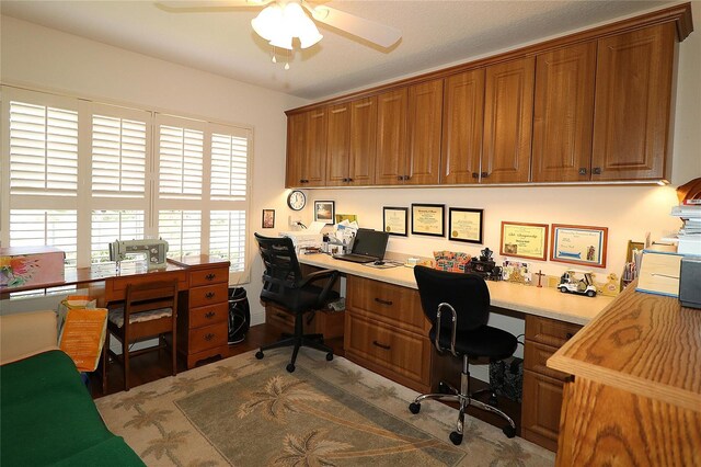 office area featuring ceiling fan, wood finished floors, and built in study area