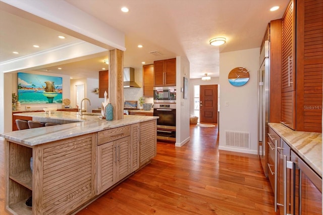 kitchen with stainless steel appliances, wall chimney range hood, beverage cooler, light wood-type flooring, and decorative backsplash