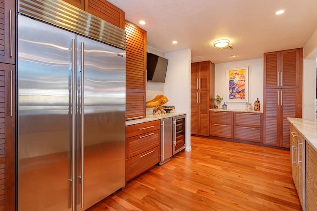 kitchen featuring built in refrigerator, brown cabinets, light wood-type flooring, wine cooler, and recessed lighting