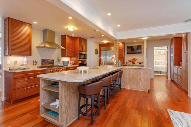 kitchen with wall chimney range hood, built in appliances, crown molding, a sink, and backsplash