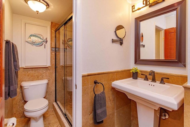 full bath with tile walls, toilet, a stall shower, a sink, and a wainscoted wall