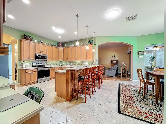 25523 Maurepas Ln, Leesburg, FL 34748 - kitchen featuring a kitchen bar, arched walkways, tasteful backsplash, visible vents, and appliances with stainless steel finishes