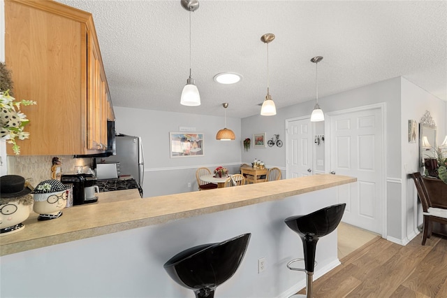 312 Emmalee Pl, The Villages, FL 32162 - kitchen with light wood-style flooring, a peninsula, a kitchen bar, a textured ceiling, and light countertops