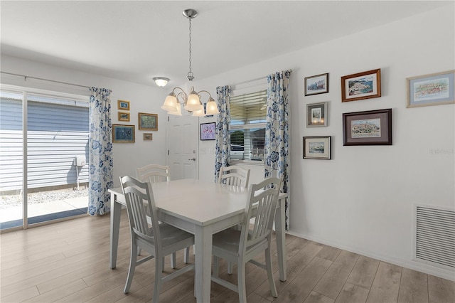 dining area with light wood-type flooring, baseboards, visible vents, and a chandelier