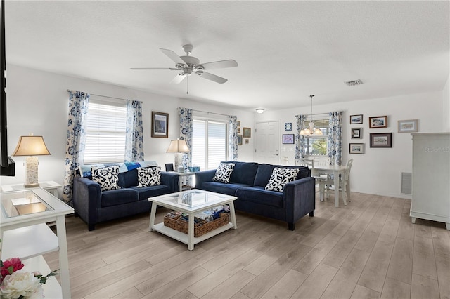 living area with light wood-style floors, visible vents, and ceiling fan with notable chandelier