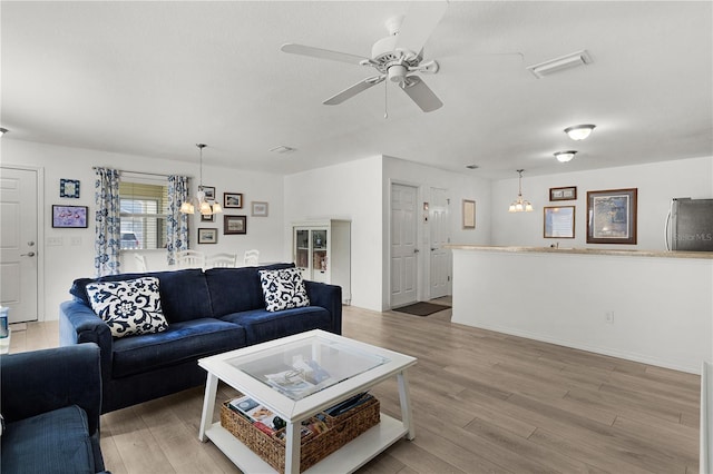 living room with light wood-type flooring, visible vents, and ceiling fan with notable chandelier