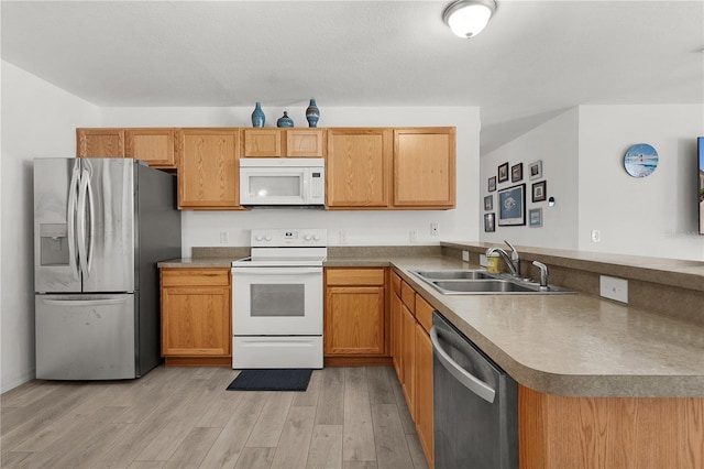 kitchen with light wood finished floors, a peninsula, a sink, and appliances with stainless steel finishes
