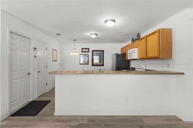 kitchen featuring wood finished floors, visible vents, white appliances, decorative light fixtures, and brown cabinetry