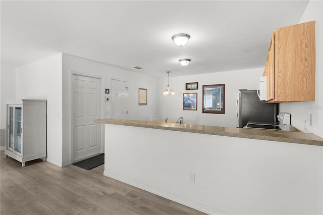 kitchen featuring light wood finished floors, a peninsula, baseboards, white microwave, and stove