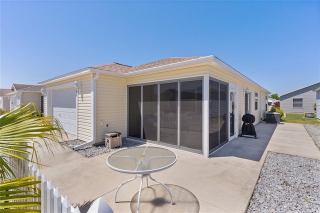 rear view of property with central air condition unit, an attached garage, roof with shingles, and a patio area