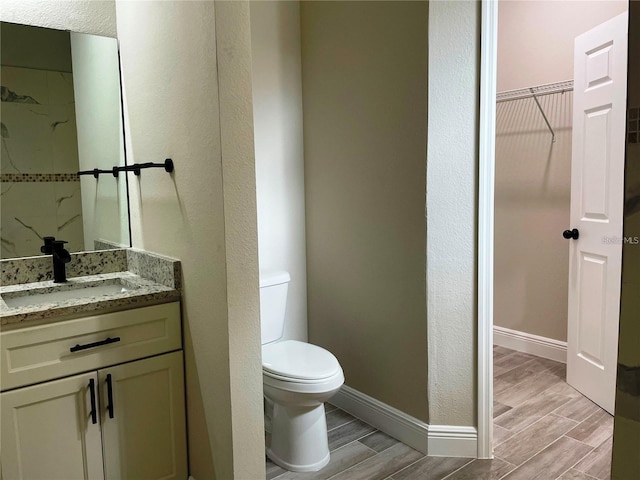 bathroom with vanity, baseboards, wood finish floors, a spacious closet, and toilet