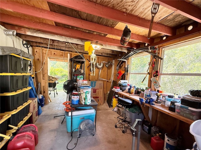 miscellaneous room featuring wooden walls, a workshop area, beam ceiling, and unfinished concrete floors