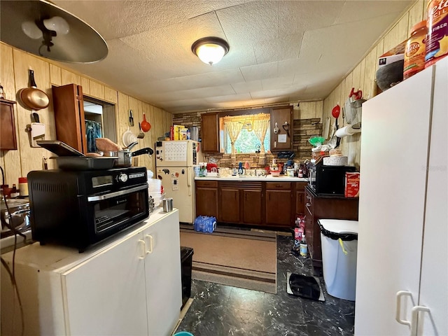 kitchen featuring a textured ceiling, wood walls, freestanding refrigerator, and a toaster