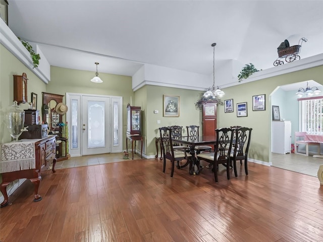 dining space with lofted ceiling, an inviting chandelier, wood-type flooring, arched walkways, and baseboards