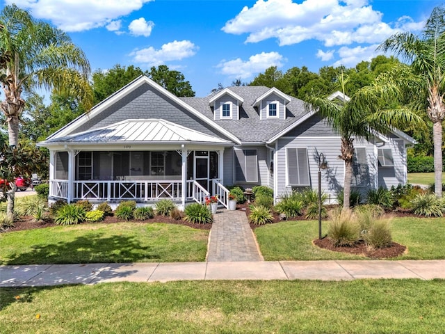view of front of house featuring a standing seam roof, a sunroom, a front yard, and roof with shingles