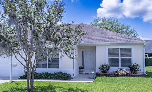 view of front of home with roof with shingles, a front lawn, a garage, and stucco siding