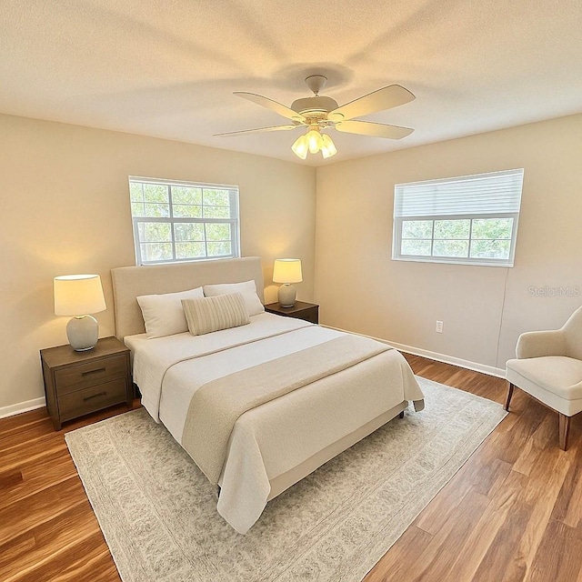 bedroom with wood finished floors, baseboards, and multiple windows