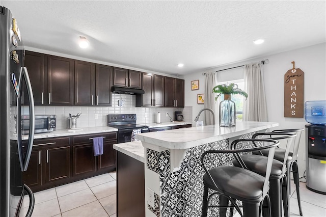 kitchen with freestanding refrigerator, light countertops, backsplash, black range with electric cooktop, and a kitchen breakfast bar