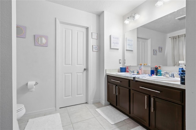 bathroom featuring tile patterned floors, toilet, double vanity, and a sink
