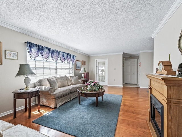 living room with a textured ceiling, baseboards, a glass covered fireplace, ornamental molding, and light wood finished floors
