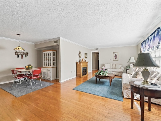 living area with a textured ceiling, crown molding, visible vents, a chandelier, and light wood-type flooring