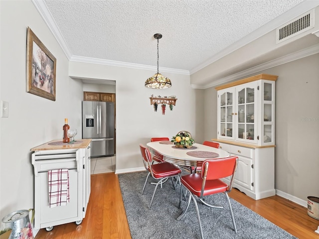dining space with a textured ceiling, crown molding, visible vents, light wood-style floors, and baseboards