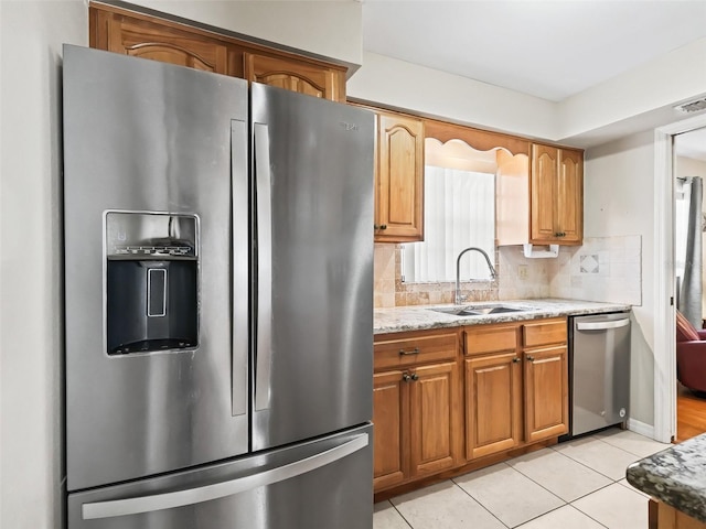 kitchen with a sink, stainless steel appliances, light tile patterned floors, tasteful backsplash, and light stone counters