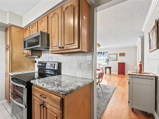 kitchen featuring decorative backsplash, brown cabinetry, appliances with stainless steel finishes, light wood finished floors, and crown molding