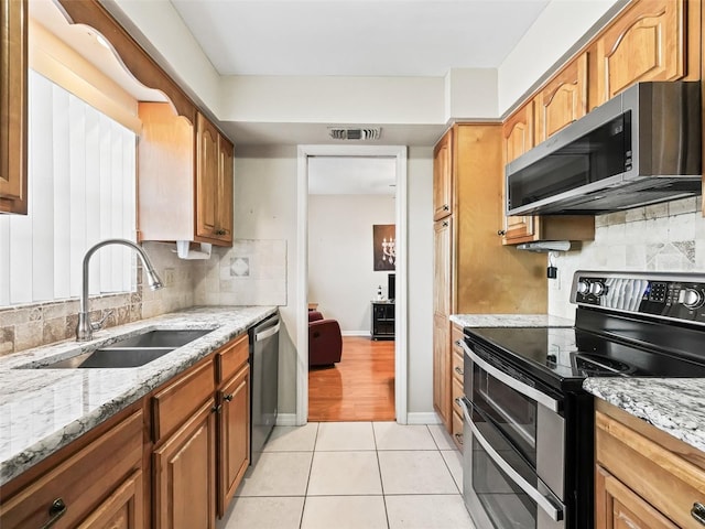 kitchen featuring light stone counters, decorative backsplash, stainless steel appliances, a sink, and visible vents