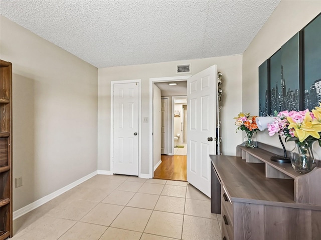 interior space with baseboards, visible vents, light tile patterned floors, and a textured ceiling